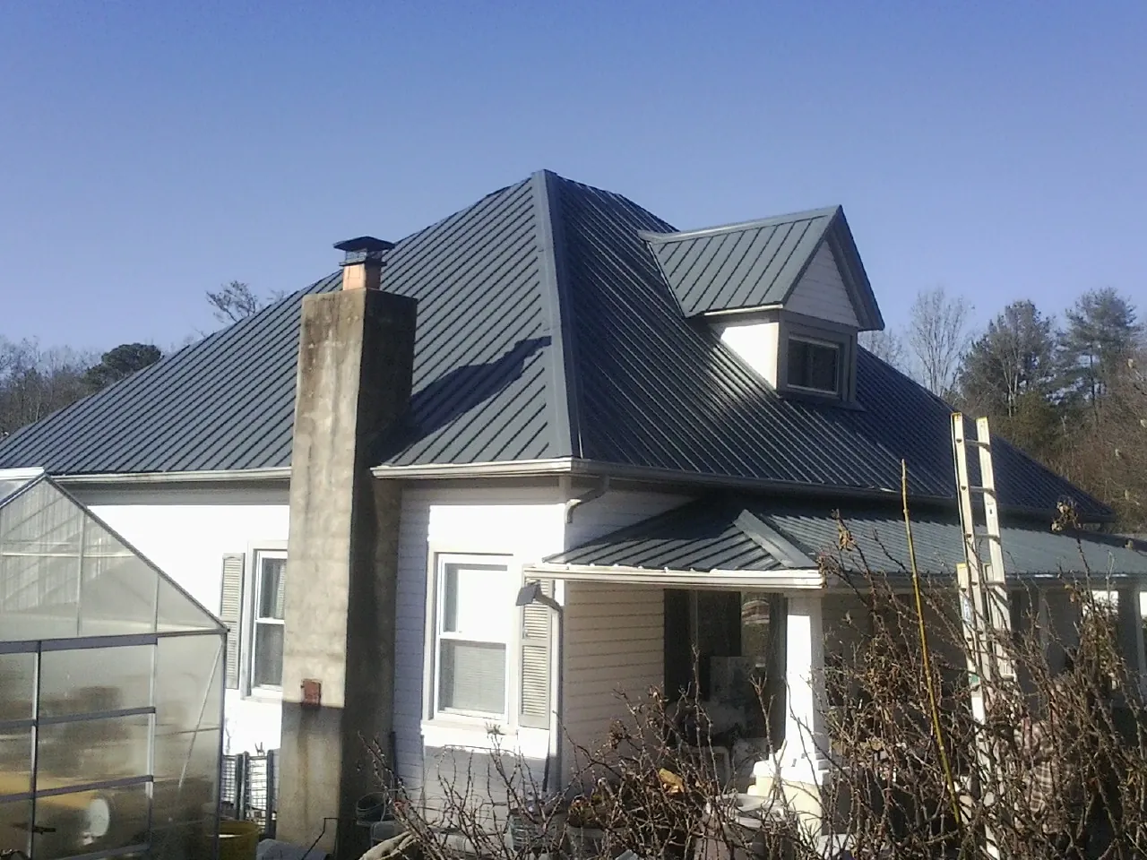 Dark blue standing seam metal roof on a white farmhouse with dormer — Slate & Tile Roof Repair by Roofing Brothers in Ray