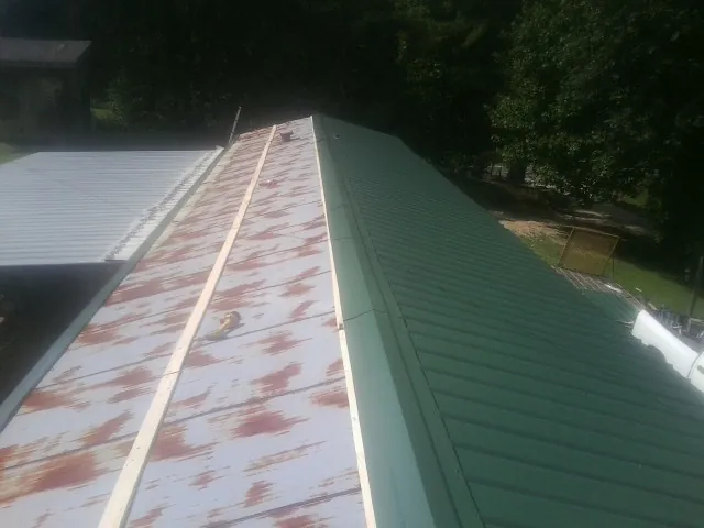 Old rusted panels beside newly installed green metal roofing — Wind Damage Roof Repair by Roofing Brothers in Ray