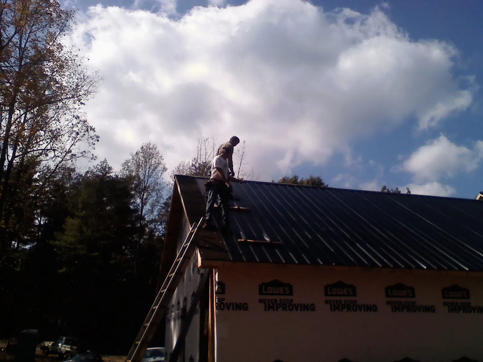 Roofer fastening dark metal panels high against a cloudy sky, from a Roof Inspection job in Ray