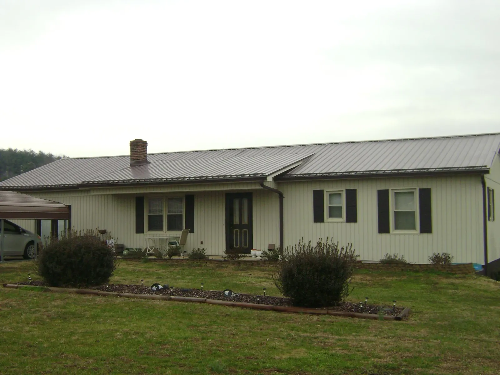 Brown metal roof on a cream sided ranch home with a brick chimney in Ray